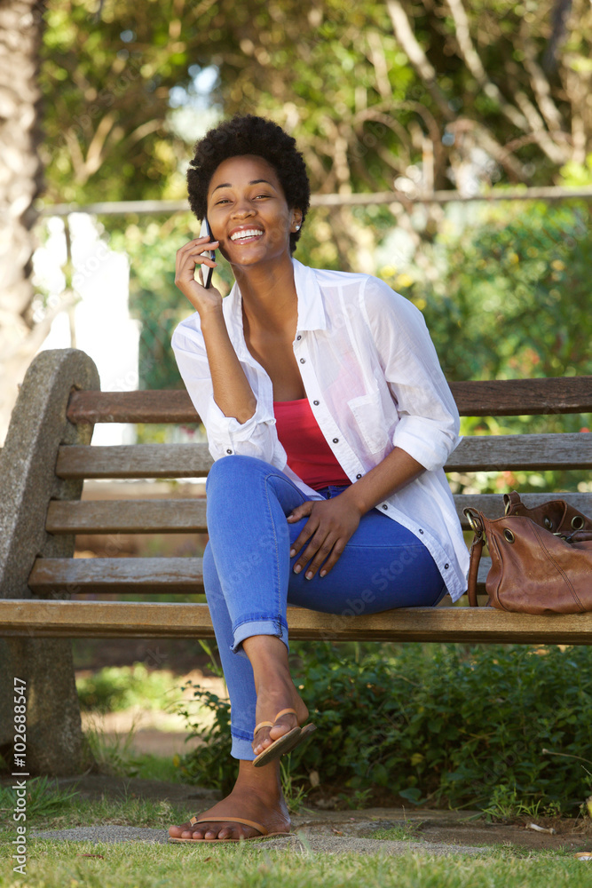 Happy young lady on a park bench and using mobile phone