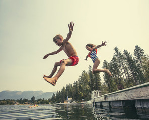 Kids jumping off the dock into a beautiful mountain lake. Having fun on a summer vacation at the lake with friends
