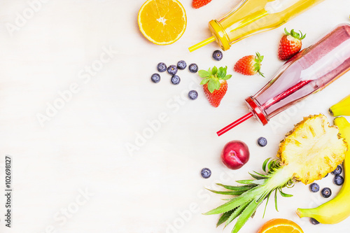 Red and yellow smoothies in bottles with fruits ingredients on white wooden background, top view, place for text. Superfoods and healthy lifestyle or detox diet food concept.