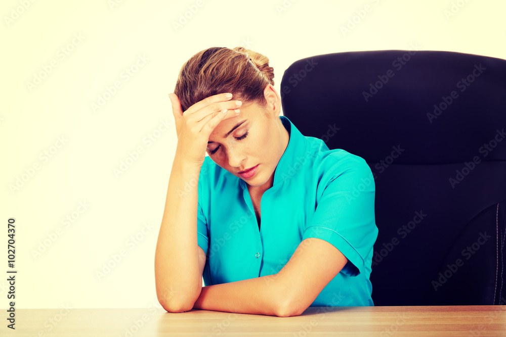 Tired young female doctoror nurse sitting behind the desk Tired young female doctoror nurse sitting behind the desk
