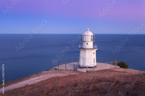 Beautiful white lighthouse on the ocean coastline at sunset. Lan