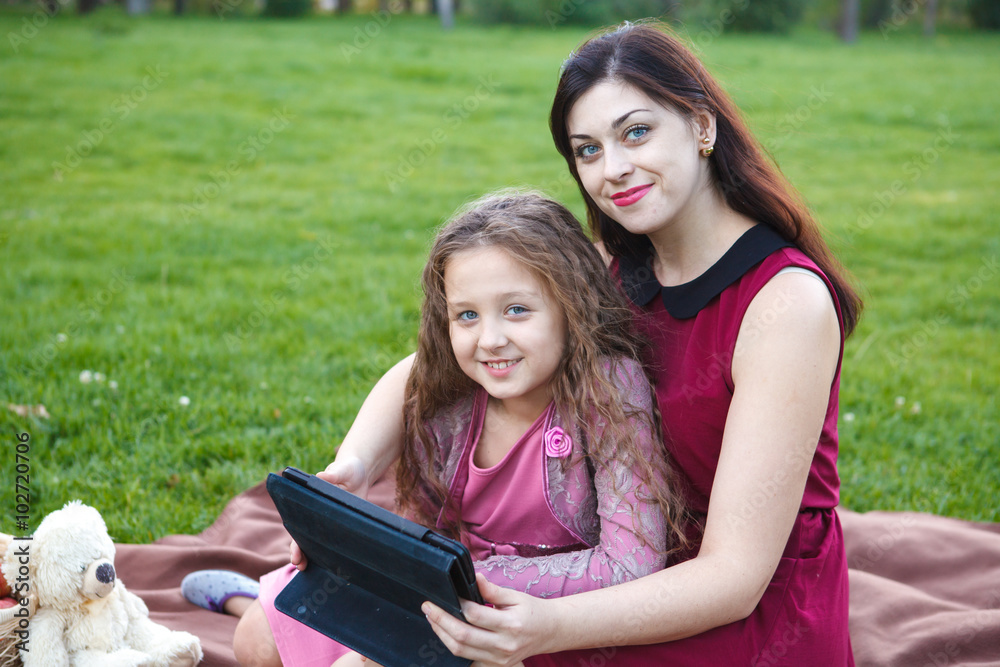Mom and daughter in the park using tablet computer Mom and daughter in the park using tablet computer