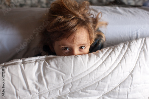 Bambina gioca a letto sotto il piumone photo