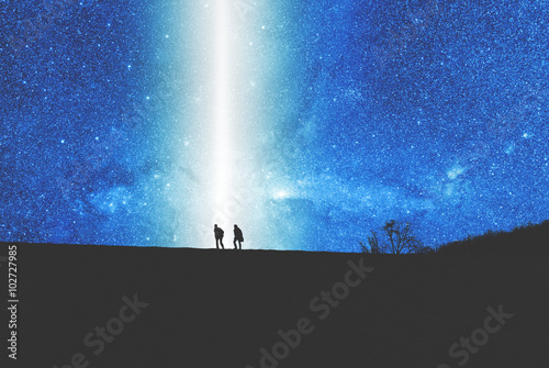 Silhouettes of two man on the top of the hill watching the stars.