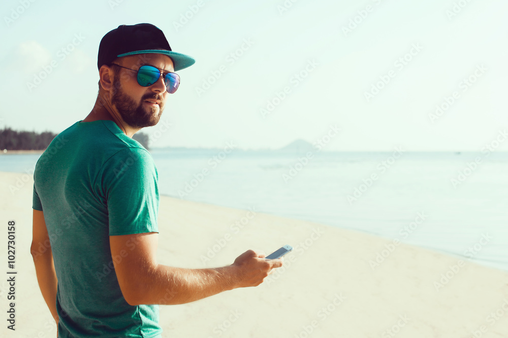 young handsome man with beard and mustache in baseball cap, surf the Internet via mobile phone, fashion smartphone are in trend, hipser style, sunglasses,outdoor portrait, close up fashion