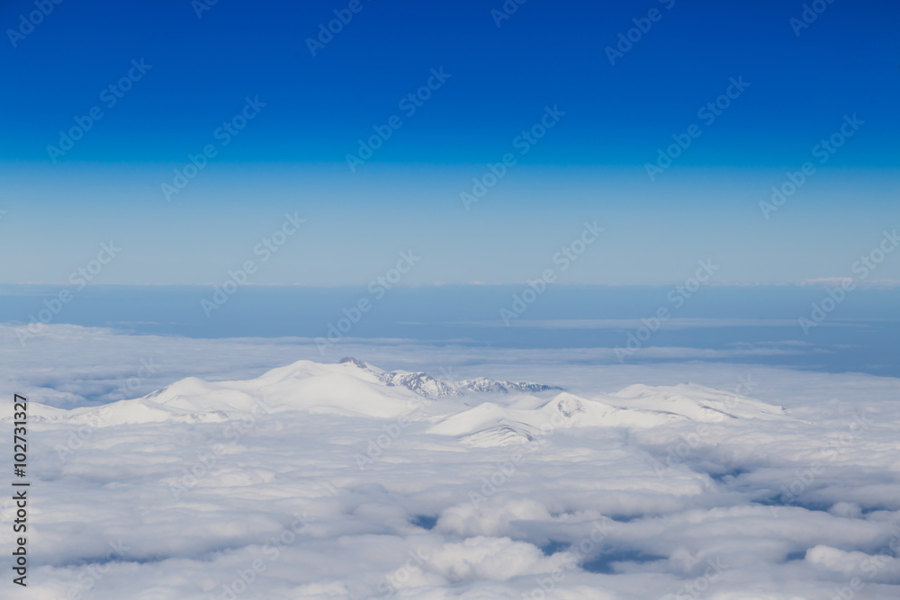 Mountain range emerging from endless white clouds, aerial shot.