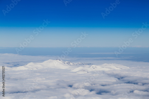 Mountain range emerging from endless white clouds  aerial shot.