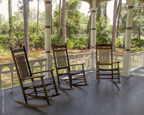 Three rocking chairs in the shade on a front porch.
