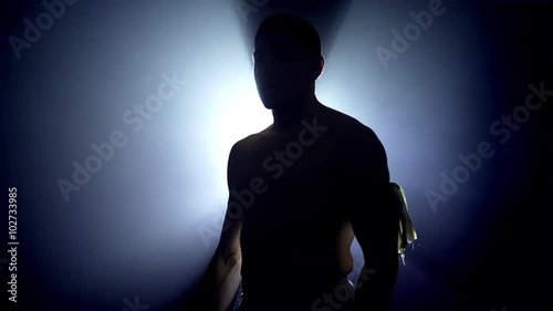 Silhouette of a triumphal Thai boxer turns around and raises his fists ready to fight, looking at camera, with a strong light behind him. UHD, 4K.
