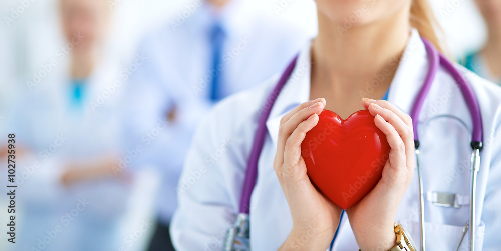 Female doctor with stethoscope holding heart - obrazy, fototapety, plakaty 
