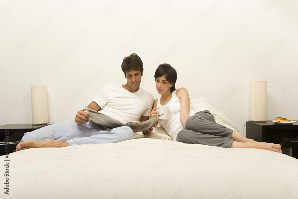 Couple on bed reading newspaper Couple on bed reading newspaper