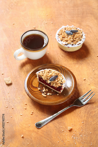 Cut of Rustic Mini Tart with Honeysuckle Curd Cream and Crumb Topping and a cup of coffee, on a wooden plate and table.