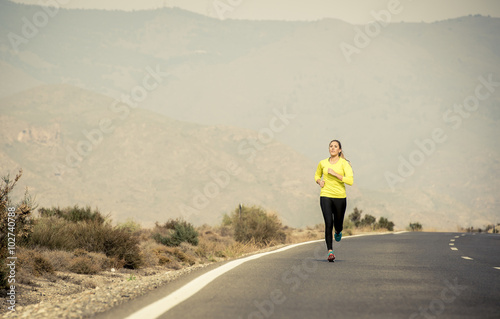 young attractive sport woman running on asphalt road with desert mountain landscape background