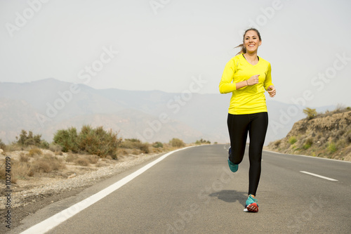 young attractive sport woman running on asphalt road with desert mountain landscape background