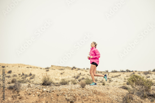 young sport woman running off road trail dirty road with dry desert landscape background training hard