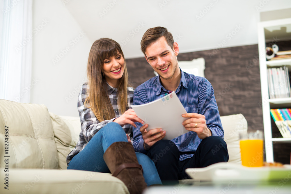 Portrait of happy couple sitting on couch and reading a magazine Portrait of happy couple sitting on couch and reading a magazine