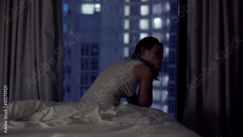 Sad, worried woman sitting at the edge of bed during night
