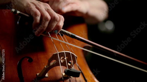 Hands and bow of a cellist playing a cello in real time.