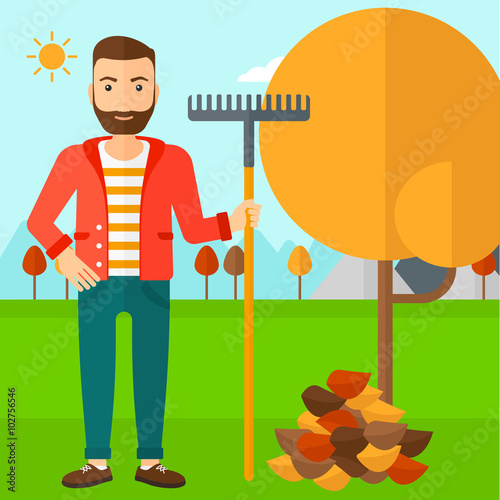 Man with rake standing near tree and heap of autumn leaves