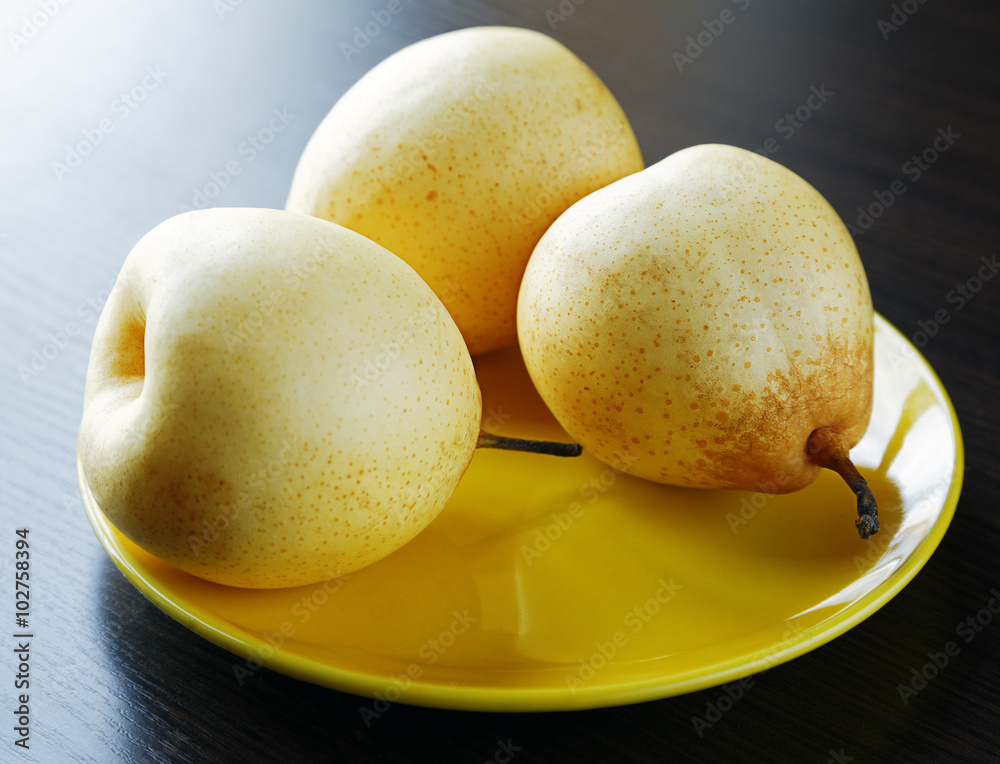 Three yellow pears on the plate on the table