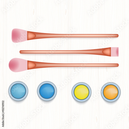 Set of colored eyeshadows and brushes on white wooden table