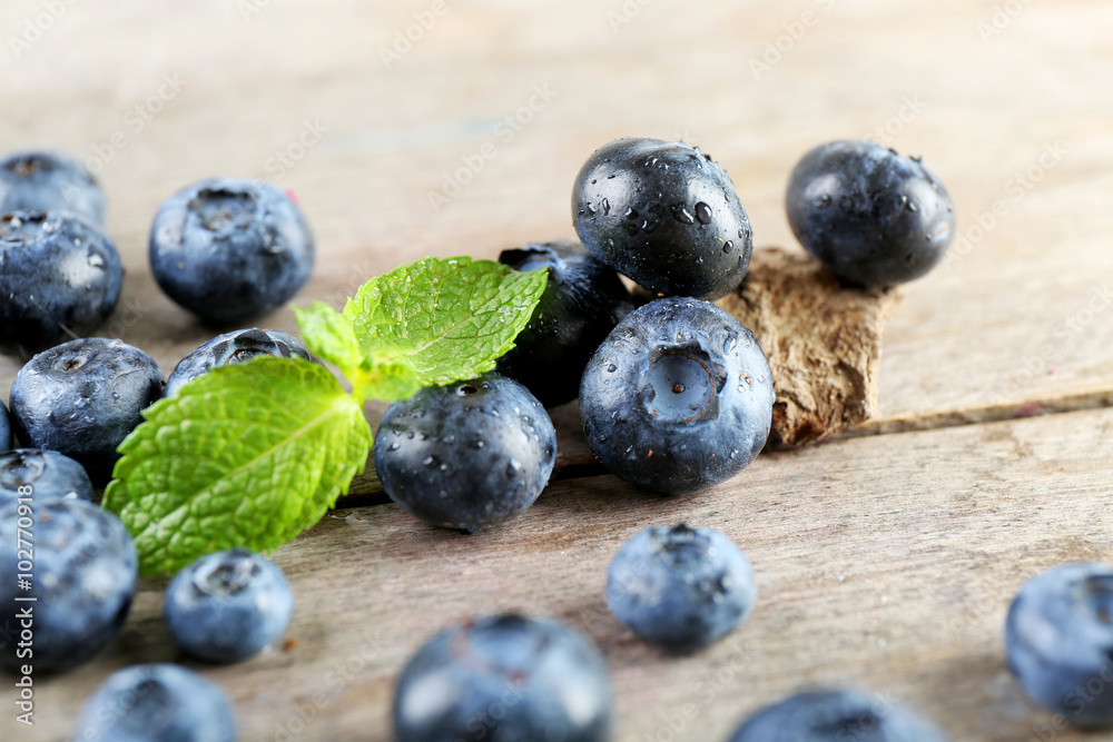 Tasty ripe blueberries with green leaves on wooden table close up Tasty ripe blueberries with green leaves on wooden table close up