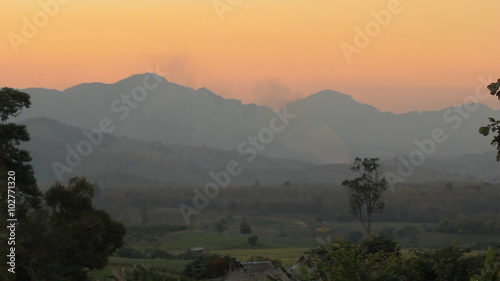 Misty mountain panorama at sunrise, with sun peeking through clouds and fog
