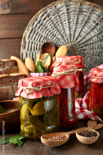 Jars with pickled vegetables and beans, spices, book of recipes and kitchen utensils on wooden background