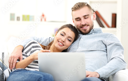 Happy couple sitting on sofa and working on a laptop © Africa Studio