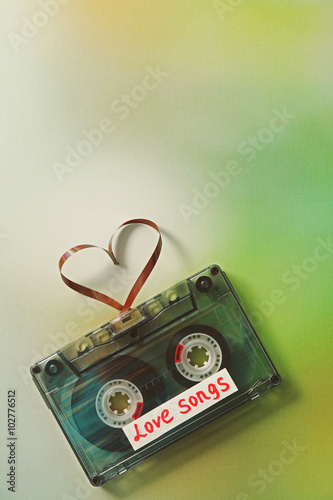 Retro audio cassette with tape in shape of heart on green blurred background