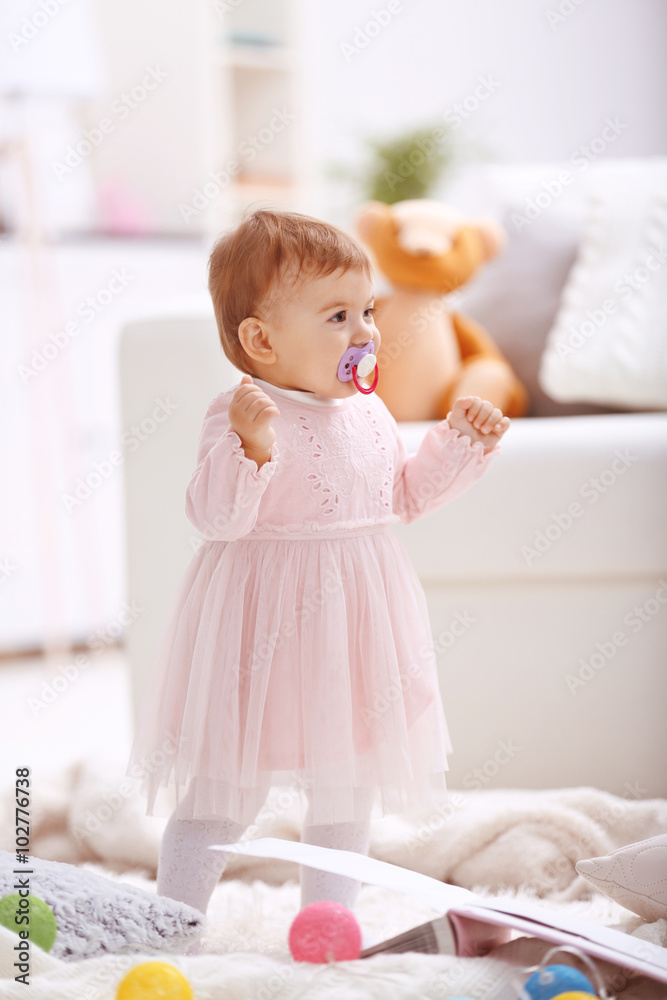 Sweet baby girl with a soother standing on floor Sweet baby girl with a soother standing on floor