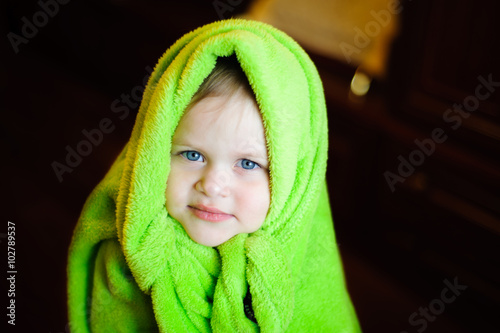 child with green fleece blanket on his head on a dark background