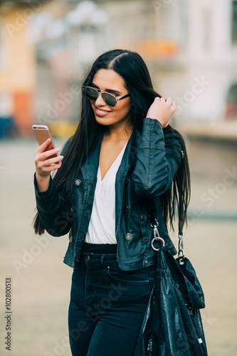 Wallpaper Mural Young beautiful casual woman texting/calling on her cell phone with sunglasses in jacket an black bag smile to camera on  spring city street. Spring outfit, Spring street look. Torontodigital.ca