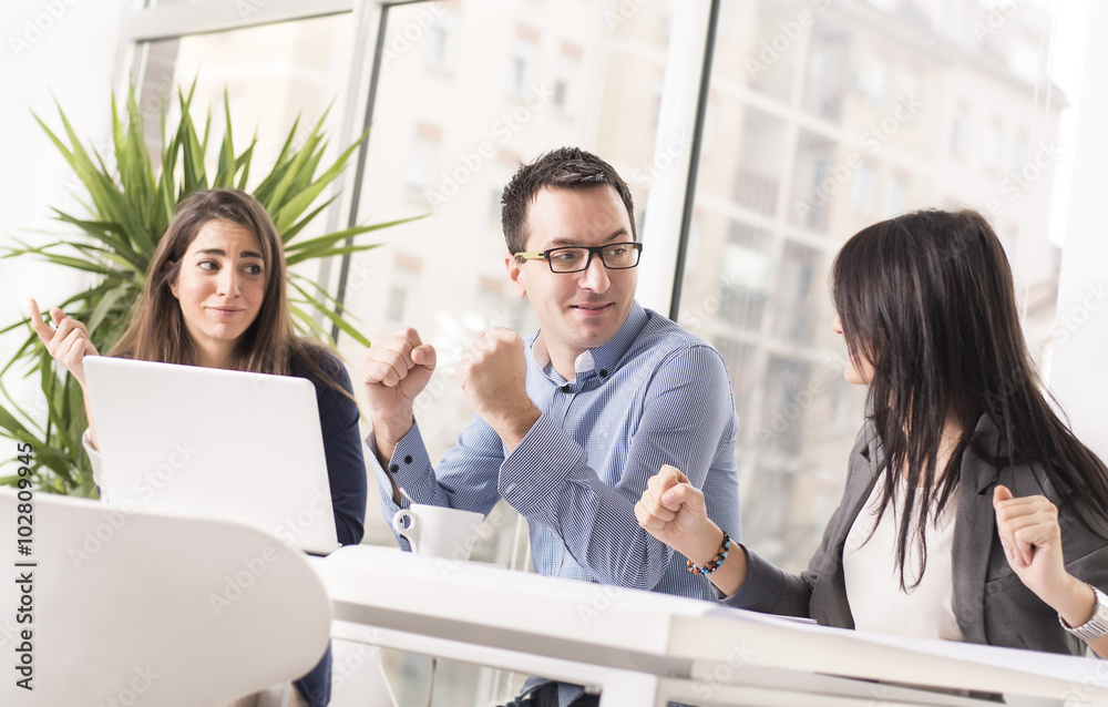 Young successful business people interacting, discussing and sharing ideas in bright modern office with clenched fists. Focus on man in the middle. Teamwork concept Young successful business people interacting, discussing and sharing ideas in bright modern office with clenched fists. Focus on man in the middle. Teamwork concept