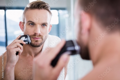 Concentrated man shaving his beard 
