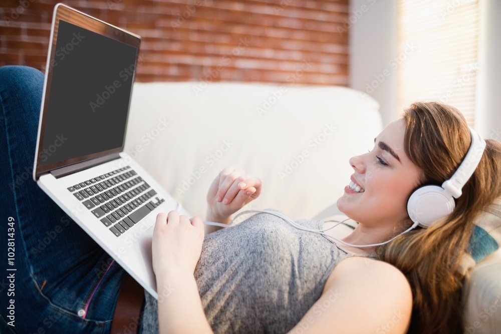 Pretty woman lying on the couch using her laptop and listening m Pretty woman lying on the couch using her laptop and listening m