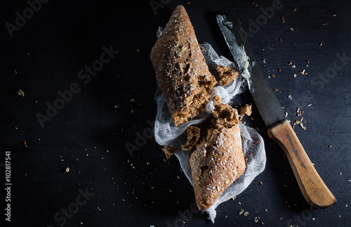Torn baguette from dark bread with seeds .and a knife smeared with butter. Top view with copy space.