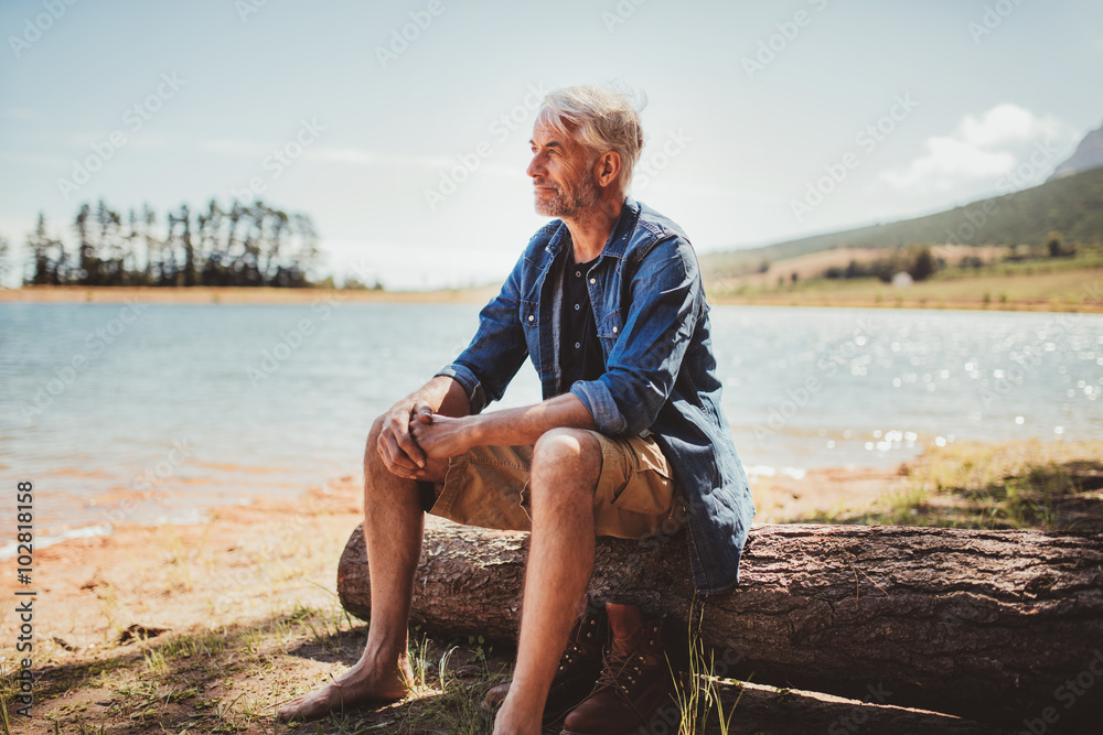 Mature man sitting on a log near lake Mature man sitting on a log near lake