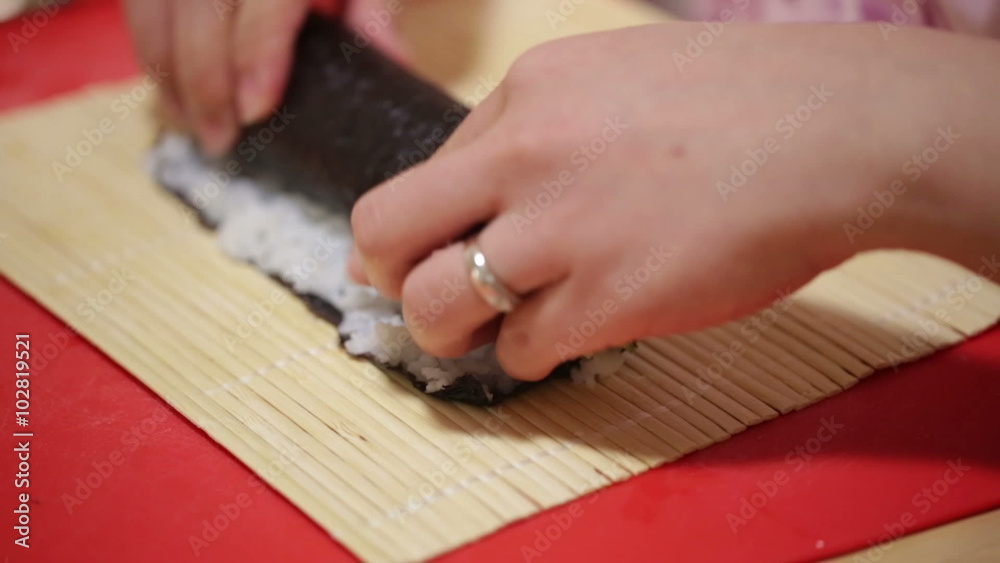 A woman prepares sushi rolls with a bamboo mat A woman prepares sushi rolls with a bamboo mat
