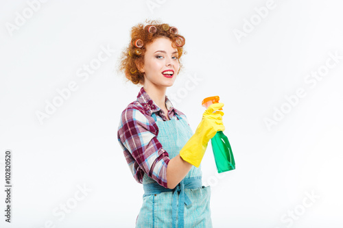 Smiling housewife in rubber gloves holding cleaning bottle and spraying