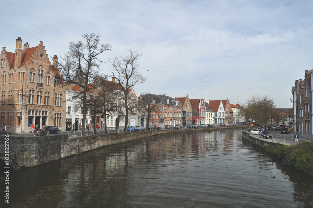 Panoramic view along one of the canals in Bruges Belgium flanked by trees and characteristic old buildings 