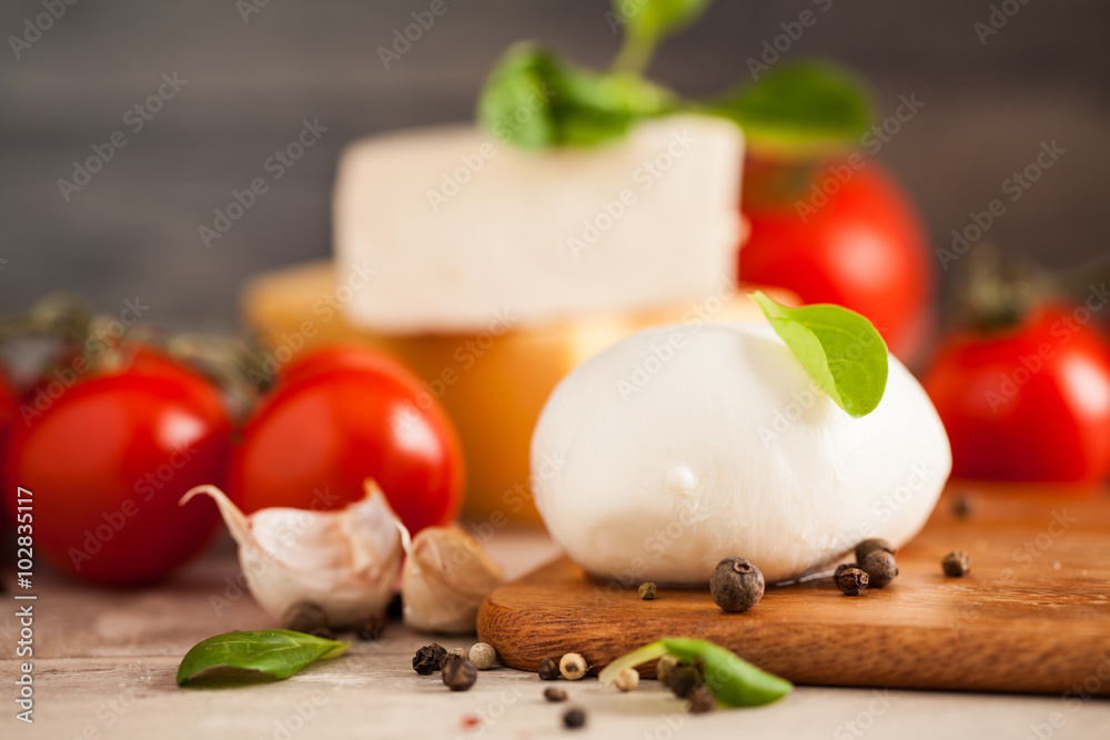 Mozzarella, organic cherry tomatoes and fresh basil on a rustic wooden background. Selective focus.