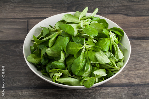 Salad leaves in bowl on wooden planks background