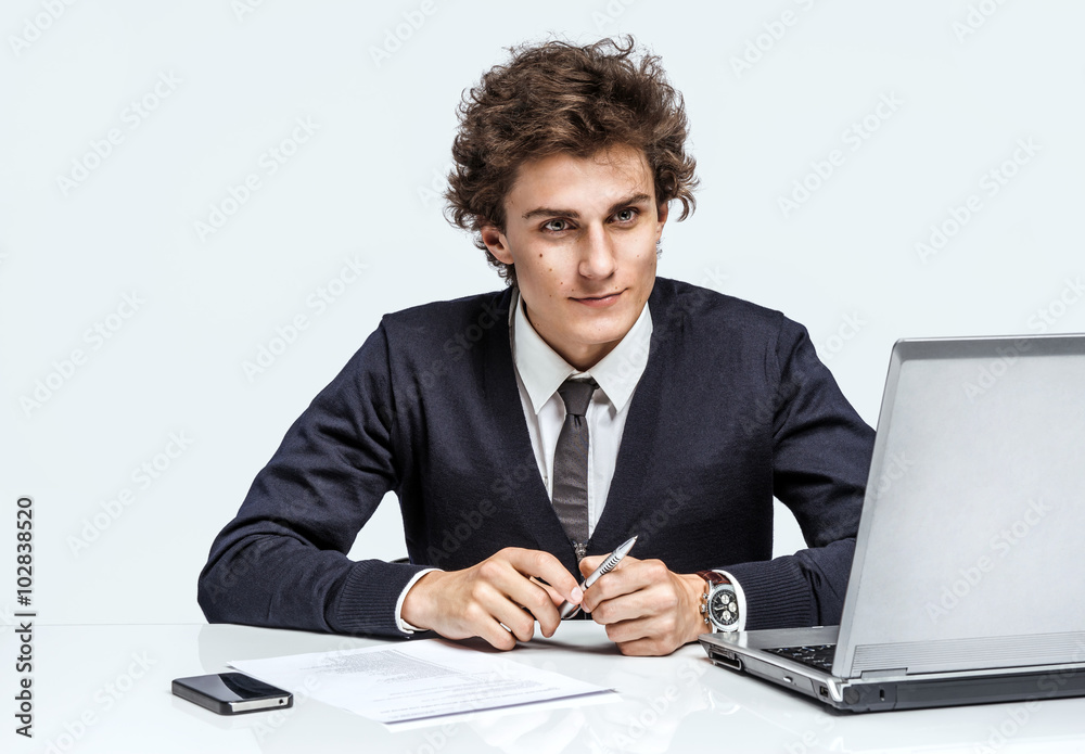 Ambitious young businessman with serious look face / businessman at the workplace working with computer on grey background. Depression and crisis concept Ambitious young businessman with serious look face / businessman at the workplace working with computer on grey background. Depression and crisis concept