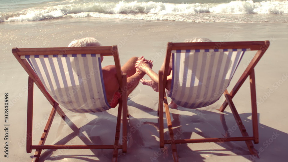 Peaceful senior couple holding hands in beach chair