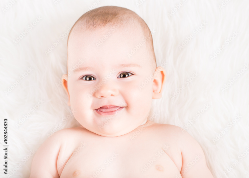 Closeup portrait of a cute smiling baby lying on white fur Closeup portrait of a cute smiling baby lying on white fur