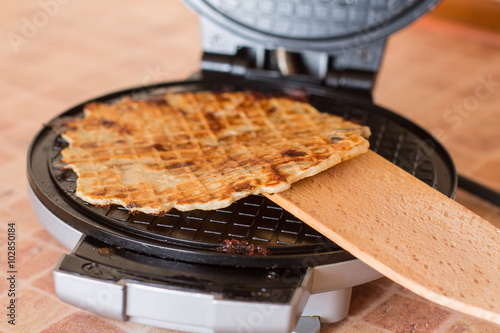 Homemade waffles with fried onions, champignons and cheese are cooked in a waffle iron with wood spatula.