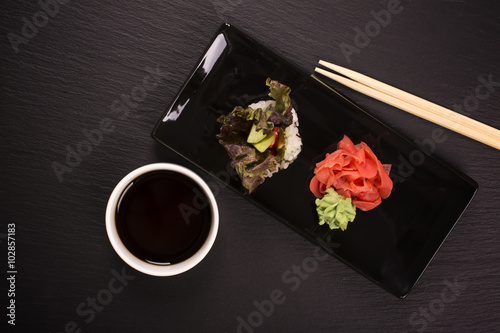Healthy japanese food concept. Vegetarian sushi roll with vegetables, soy sauce, and chopsticks over black stone table. Selective focus