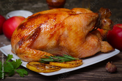 whole chicken noticed roasted with lemon and apples on a plate on a wooden background