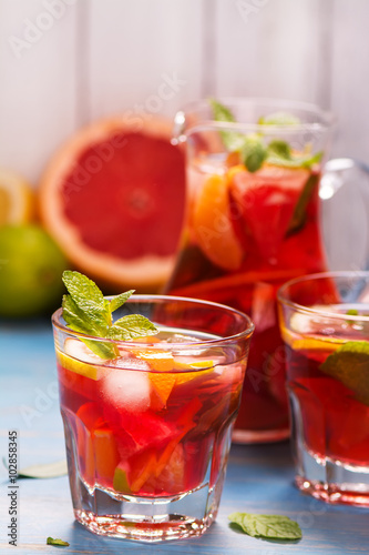 Jug and glasses with homemade citrus lemonade with mint and ice cubes over wooden background. Selective focus